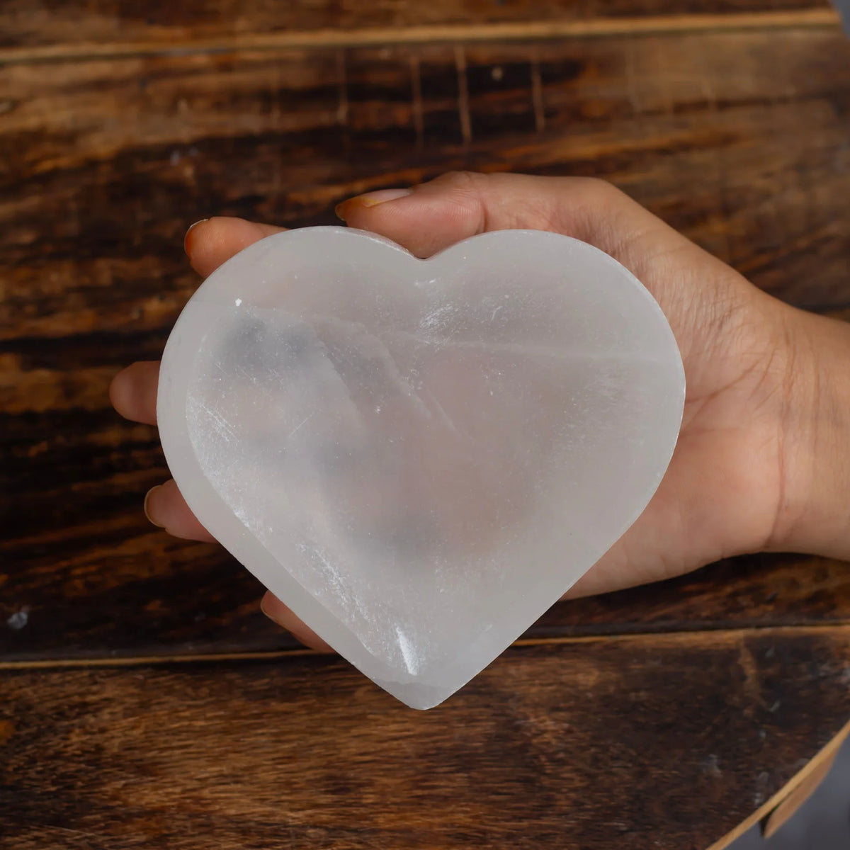 Heart shaped selenite charging bowl displayed in a dark, softly lit spiritual setting