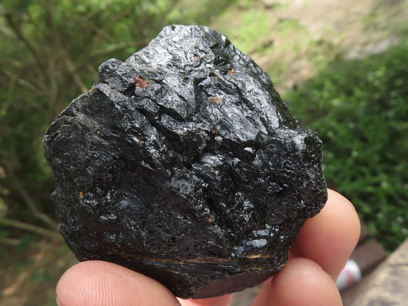 Hand holding one large rough black tourmaline stone outdoors to show natural texture