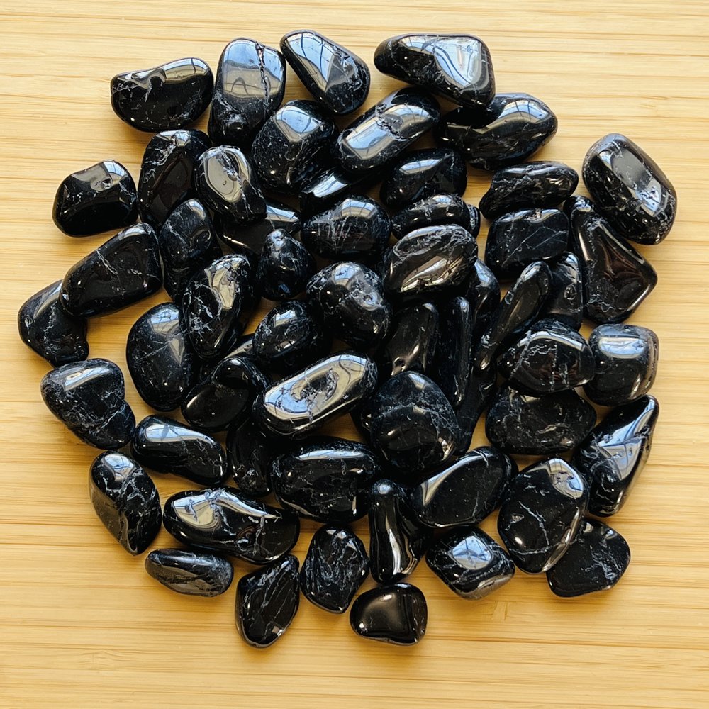 Pile of polished black tourmaline stones spread on a wooden surface