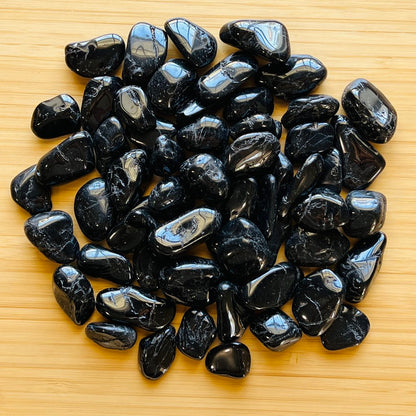 Pile of polished black tourmaline stones spread on a wooden surface