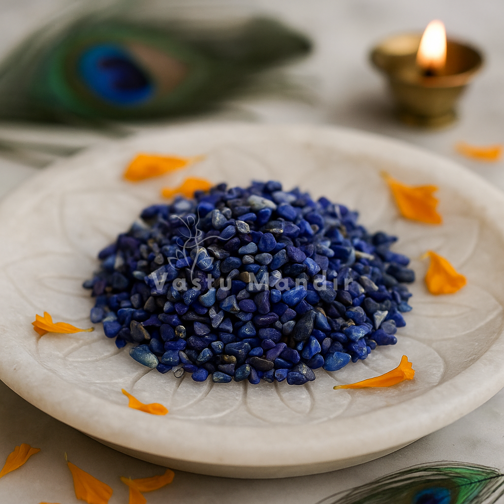 Angled view of lapis lazuli crystal chips on a white plate with marigold petals and a peacock feather