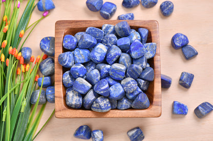 Lapis lazuli stones arranged in a small wooden tray with blue flowers beside them
