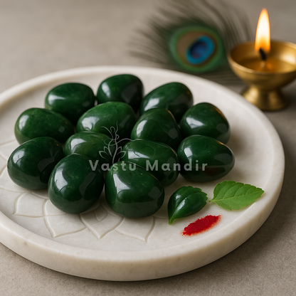 Green jade tumbled stones arranged on a carved white plate with marigold petals and a softly lit diya