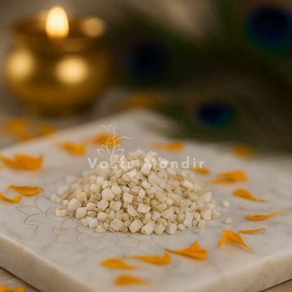 Angled view of white calcite crystal chips on a white plate with marigold petals and a peacock feather