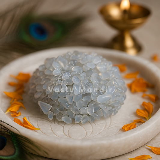 Opalite crystal chips arranged on a carved white plate with marigold petals and a softly lit diya