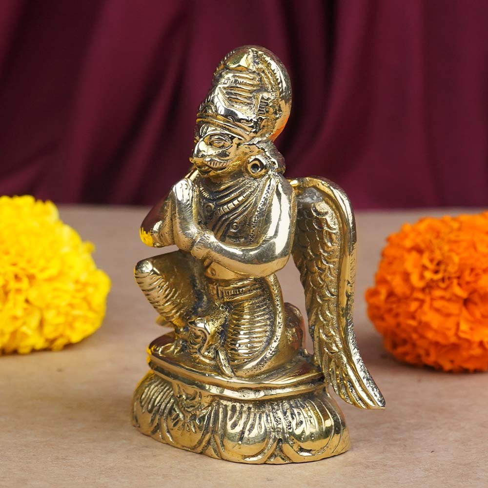 Brass Lord Garud Dev Ji idol displayed against burgundy drapery with marigold flowers