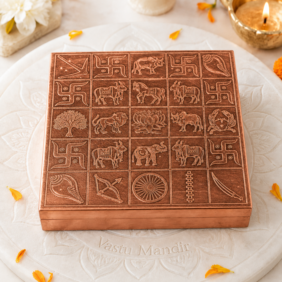 Copper Manjusha box on a white plate with orange petals and a lit candle