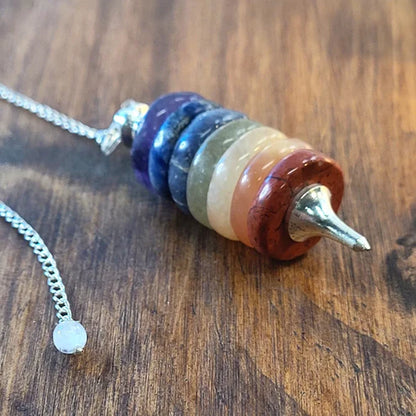 Close-up of multicolour gemstone seven chakra pendulum with silver chain on wood