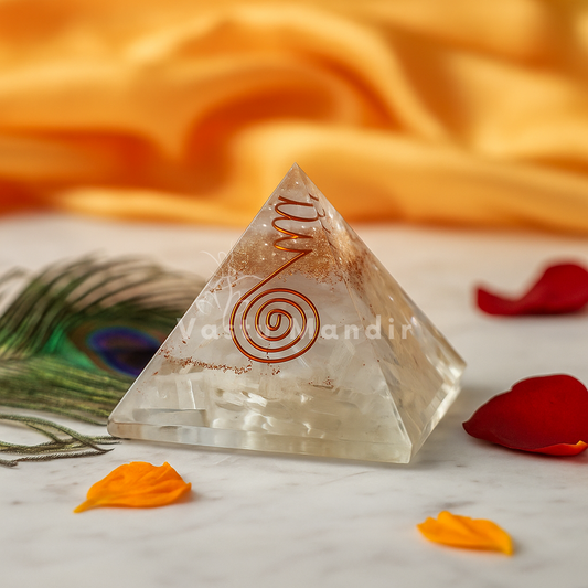 Crystal pyramid with spiral design on a marble surface with peacock feather and petals.