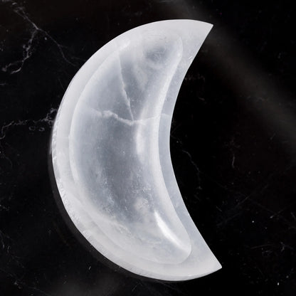 Cresent moon selenite charging bowl presented against a dark decorative backdrop