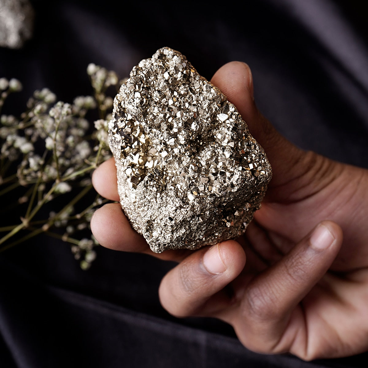 Hand holding a rough silver-grey pyrite cluster against a dark background
