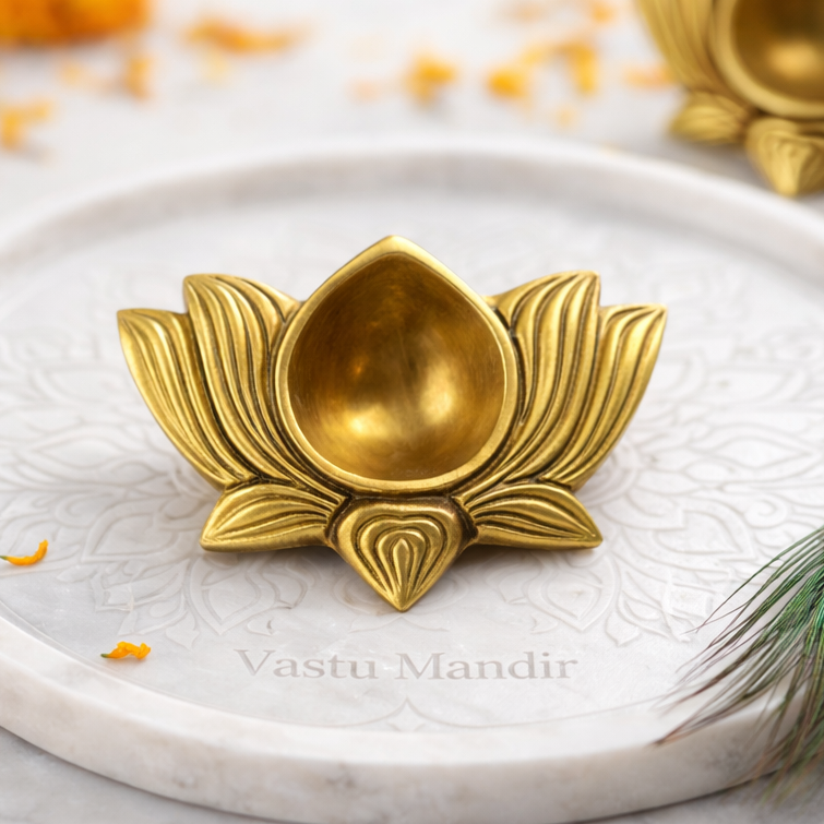 Small Brass Lotus Diya on a white plate with marigold flowers and a peacock feather.