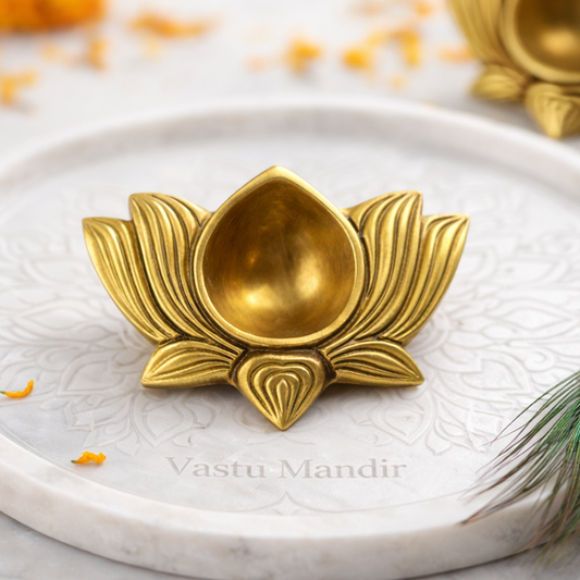 Small Brass Lotus Diya on a white plate with marigold flowers and a peacock feather.