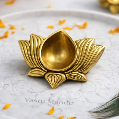 Brass lotus-shaped diya on a marble plate with marigold flowers and a peacock feather.