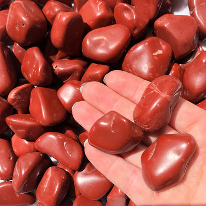 Hand holding several red jasper tumbled stones outdoors to show natural colour, scale and texture