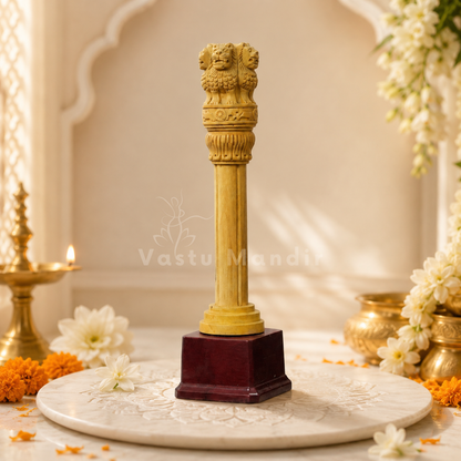 A decorative Wooden Ashoka pillar with a lion capital on top, mounted on a dark reddish-brown square base, displayed on a marble tray with floral and brass decorative elements.