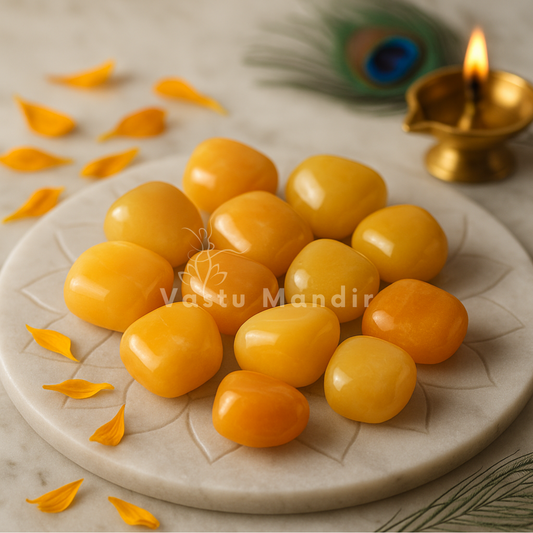 Yellow jade tumbled stones arranged on a carved white plate with marigold petals and a softly lit diya
