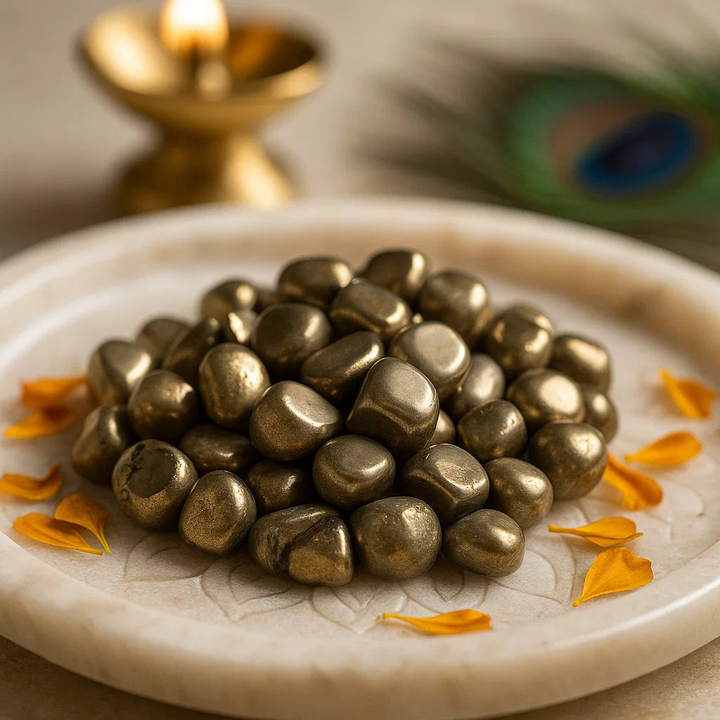 Wide view of golden pyrite tumbled stones displayed on a white plate with brass decor and flower petals