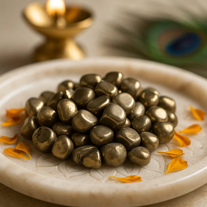 Wide view of golden pyrite tumbled stones displayed on a white plate with brass decor and flower petals