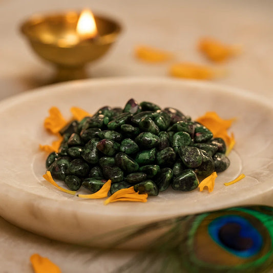 Ruby zoisite chips arranged on a carved white plate with marigold petals and a softly lit diya
