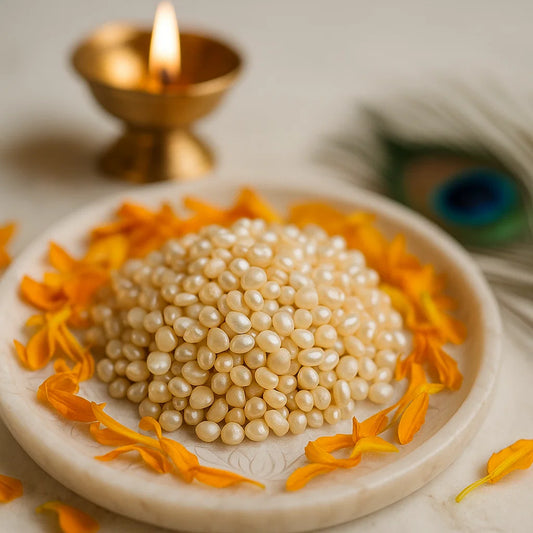 Round cream pearl beads arranged on a white plate with marigold petals and a softly lit diya