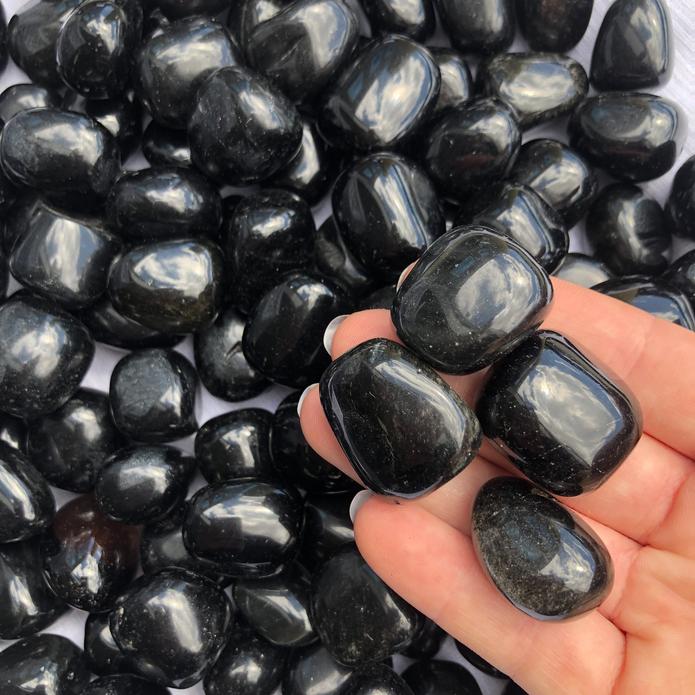 Hand holding several polished black tourmaline stones for a close view of their finish