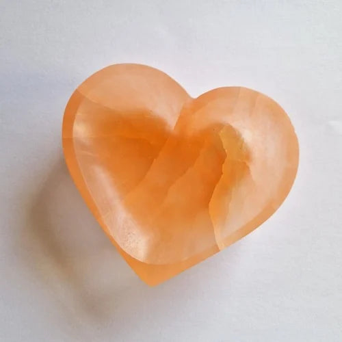 Orange heart selenite charging bowl arranged in a styled spiritual setting