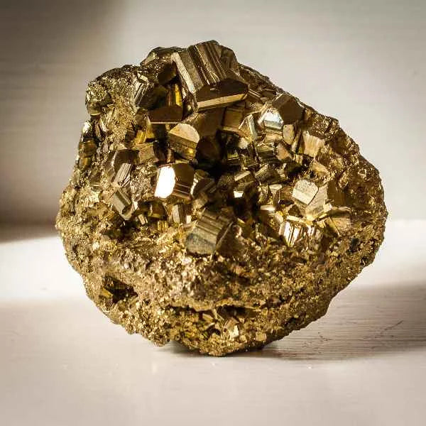 Golden cubic pyrite cluster shown close-up on a neutral beige surface