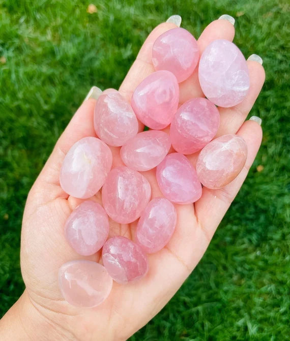Hand holding several rose quartz tumbled stones outdoors to show natural colour, scale and texture