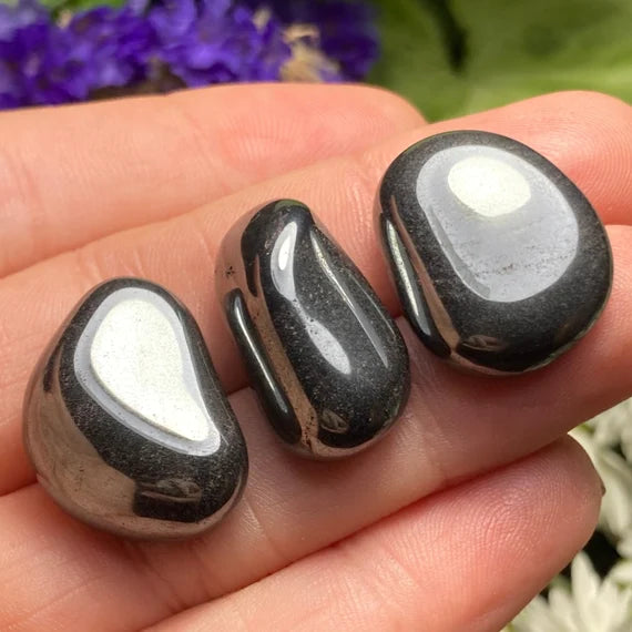 Hand holding several hematite tumbled stones outdoors to show natural colour, scale and texture