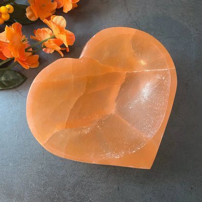 Orange heart selenite charging bowl displayed in a softly lit product setting