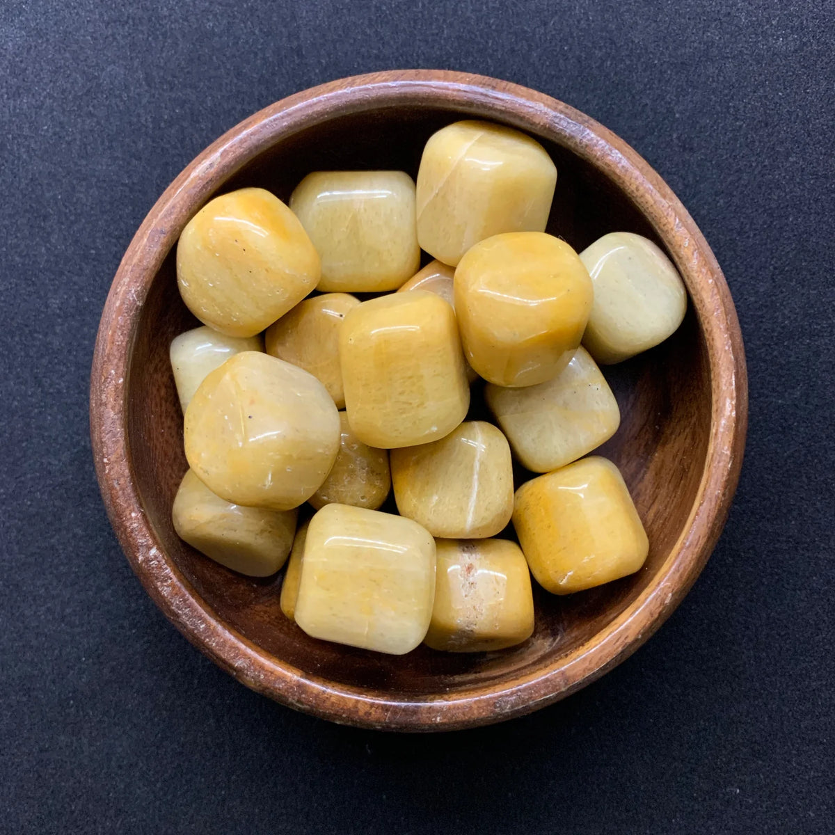 Yellow jade tumbled stones displayed in a small bowl with a neutral background