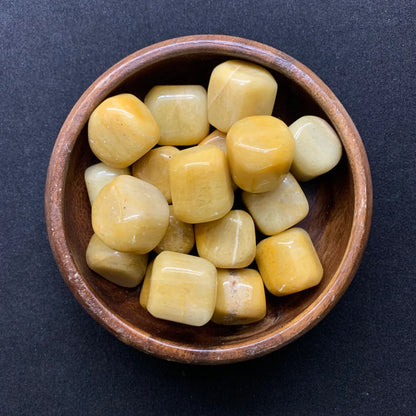 Yellow jade tumbled stones displayed in a small bowl with a neutral background