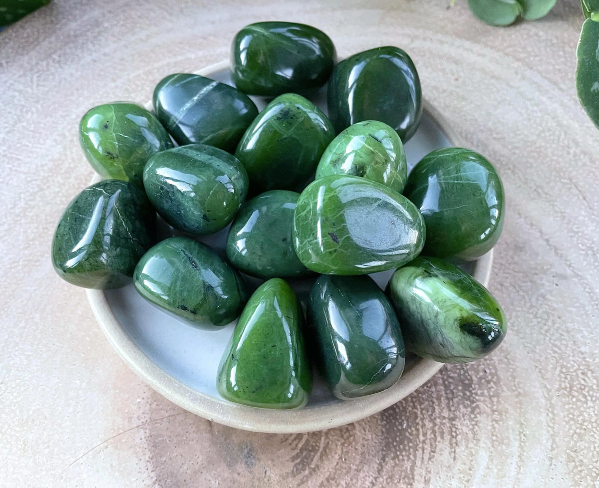 Green jade tumbled stones displayed in a small bowl with a neutral background