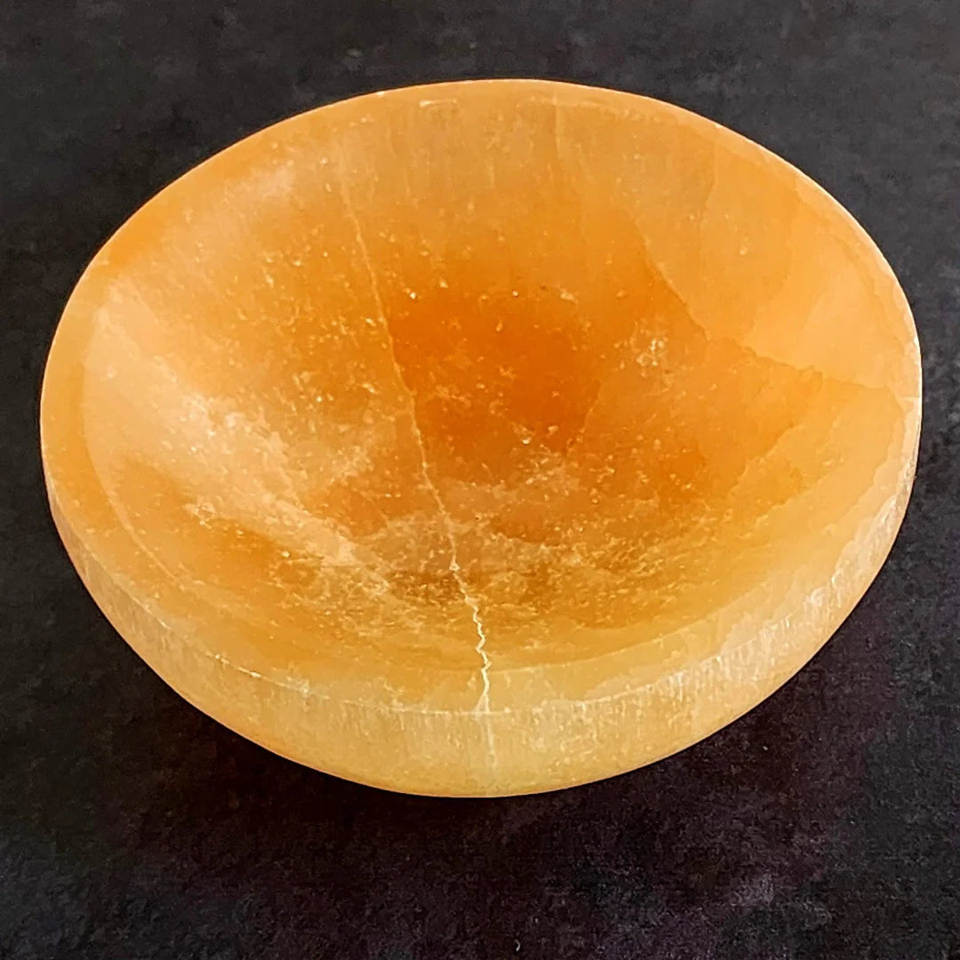 Orange round selenite charging bowl shown in a close atmospheric product view