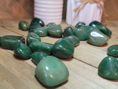 Green jade tumbled stones spread on a wooden surface in natural light