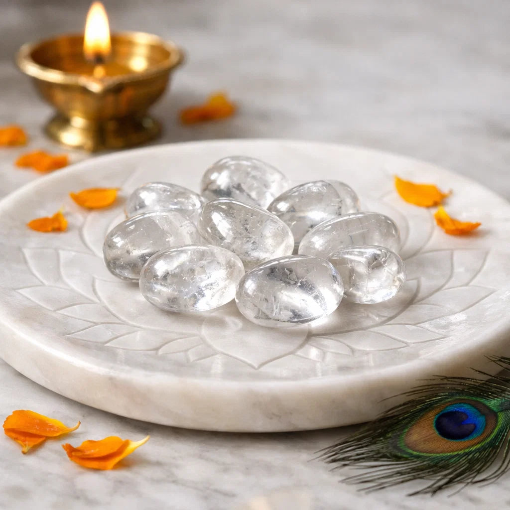 Wide view of clear quartz tumbled stones displayed on a white plate with brass decor and flower petals