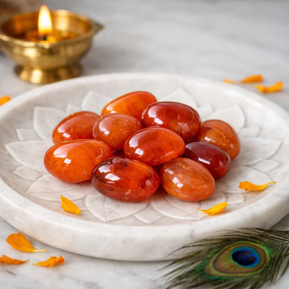 Close front view of carnelian tumbled stones on a carved white plate with marigold petals