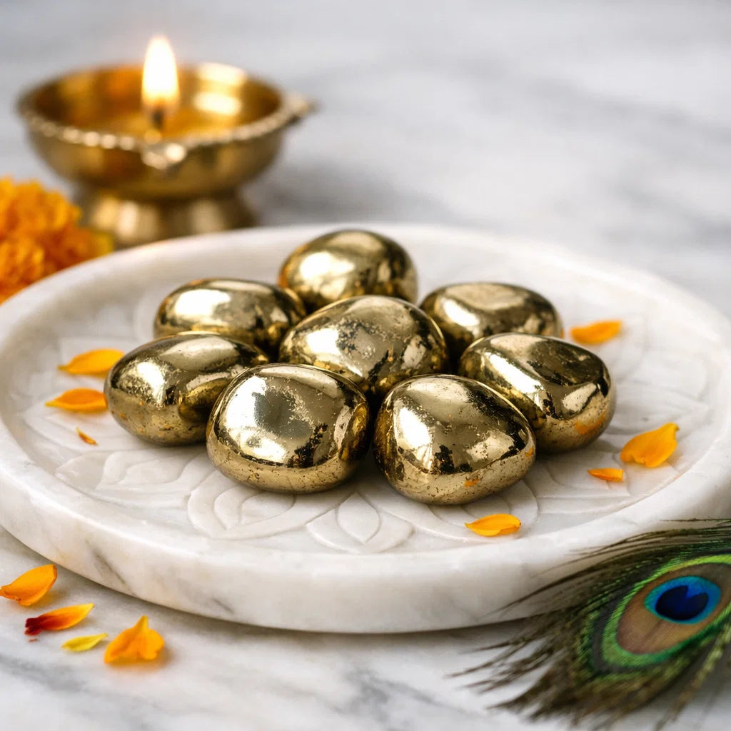 Angled view of golden pyrite tumbled stones on a white plate with marigold petals and a peacock feather
