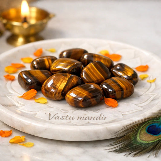 Tiger eye tumbled stones arranged on a carved white plate with marigold petals and a softly lit diya
