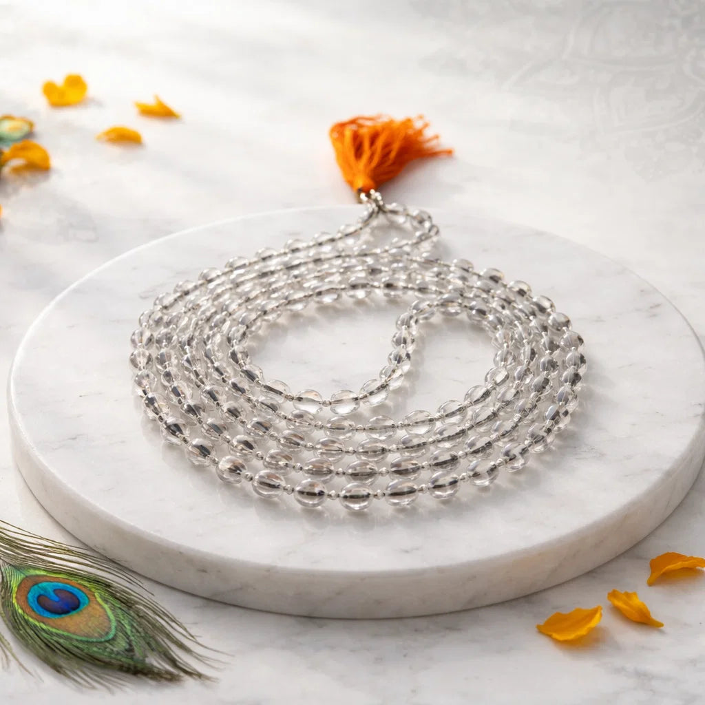 Sphatik crystal mala arranged with a central loop and orange tassel on a white plate