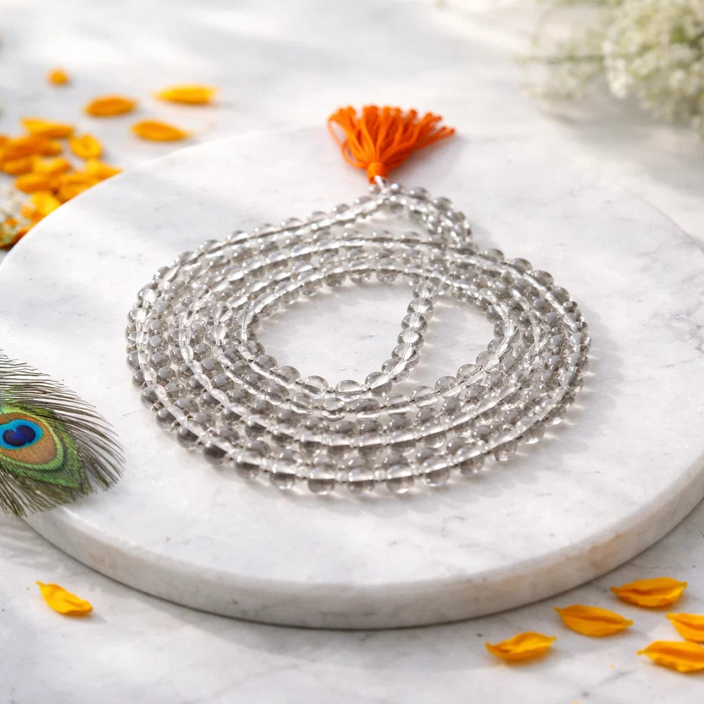 Clear sphatik mala arranged in a long coil on a white plate with peacock feather decor
