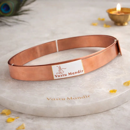 Pure copper Vastu strip coil on a branded plate with petals and a blurred diya