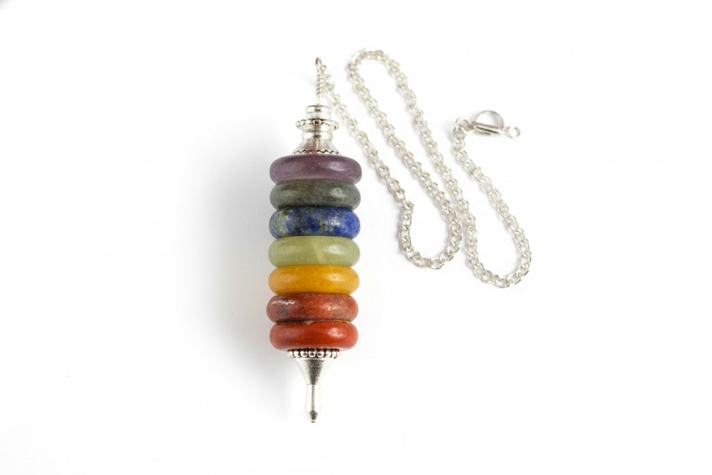 Seven chakra pendulum hanging from its silver chain on a white background